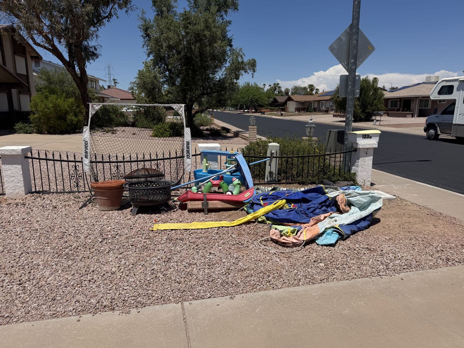 Curbside pile of backyard toys, a fire pit, and yard gear staged at a Mesa driveway for bulk pickup