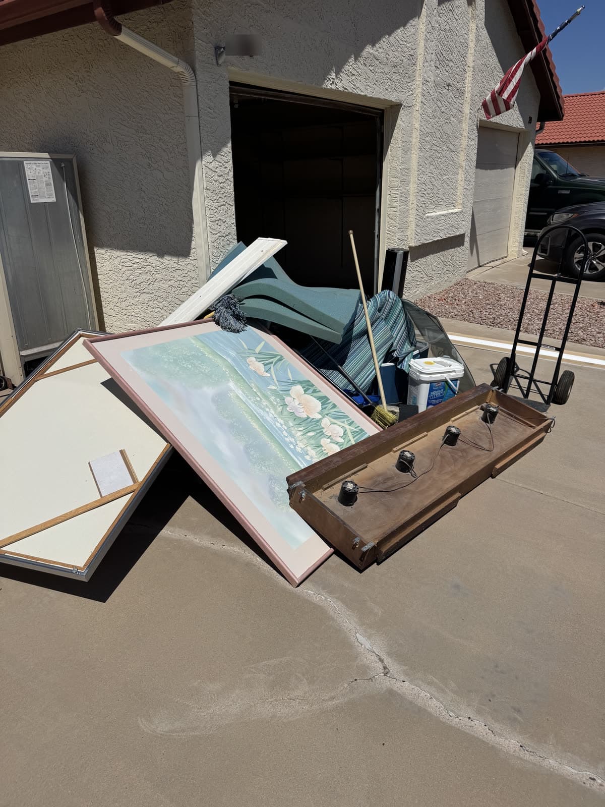 Interior doors, a framed picture, a mattress, and patio cushions staged in a driveway for junk removal pickup