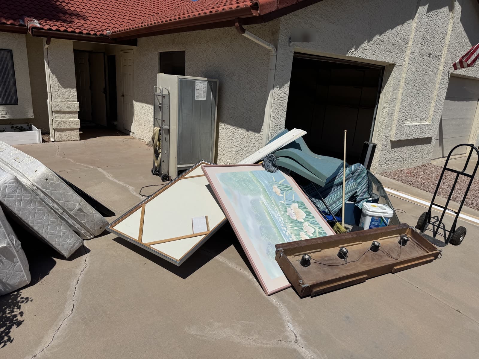 Wide view of doors, mattresses, and a cabinet staged at a garage with a hand truck ready for loading