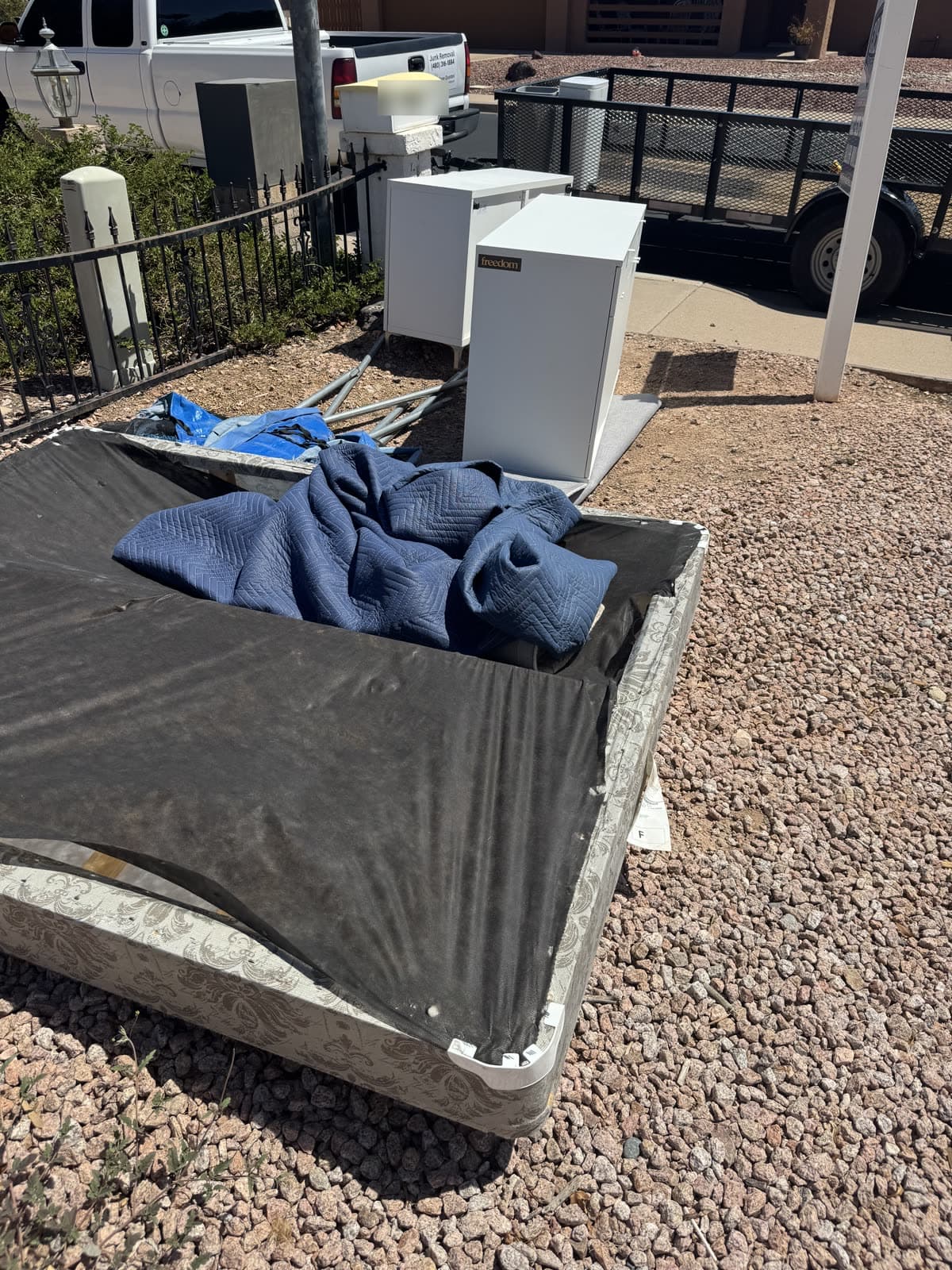 Box spring, mattress, and two white cabinets at the curb with the trailer behind