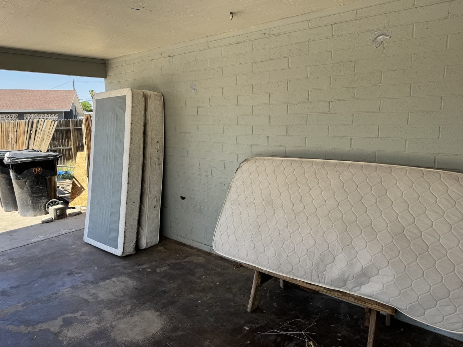 Three mattresses and box springs leaning in a carport waiting for pickup
