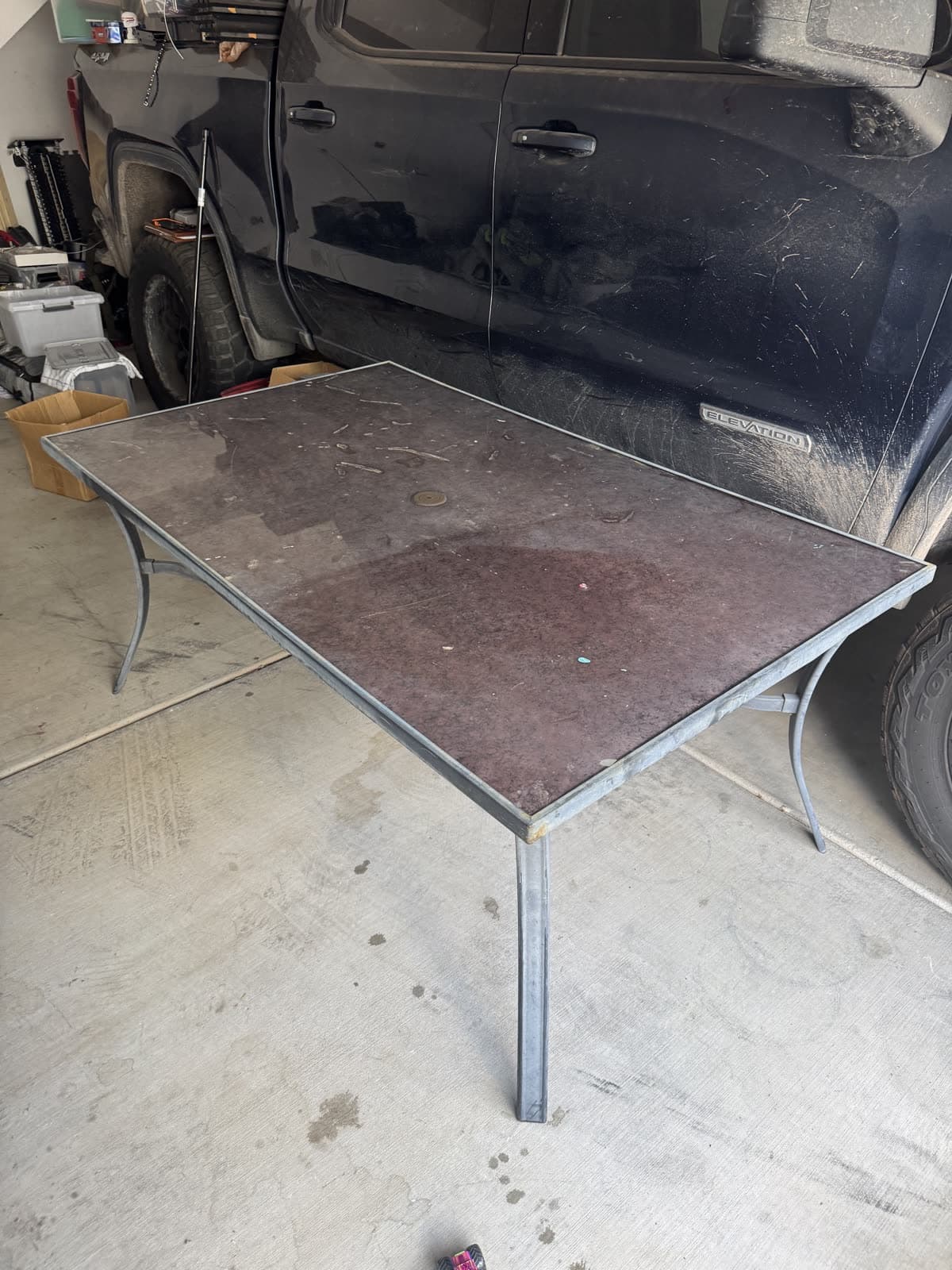 Worn patio table in a driveway next to the pickup truck before removal