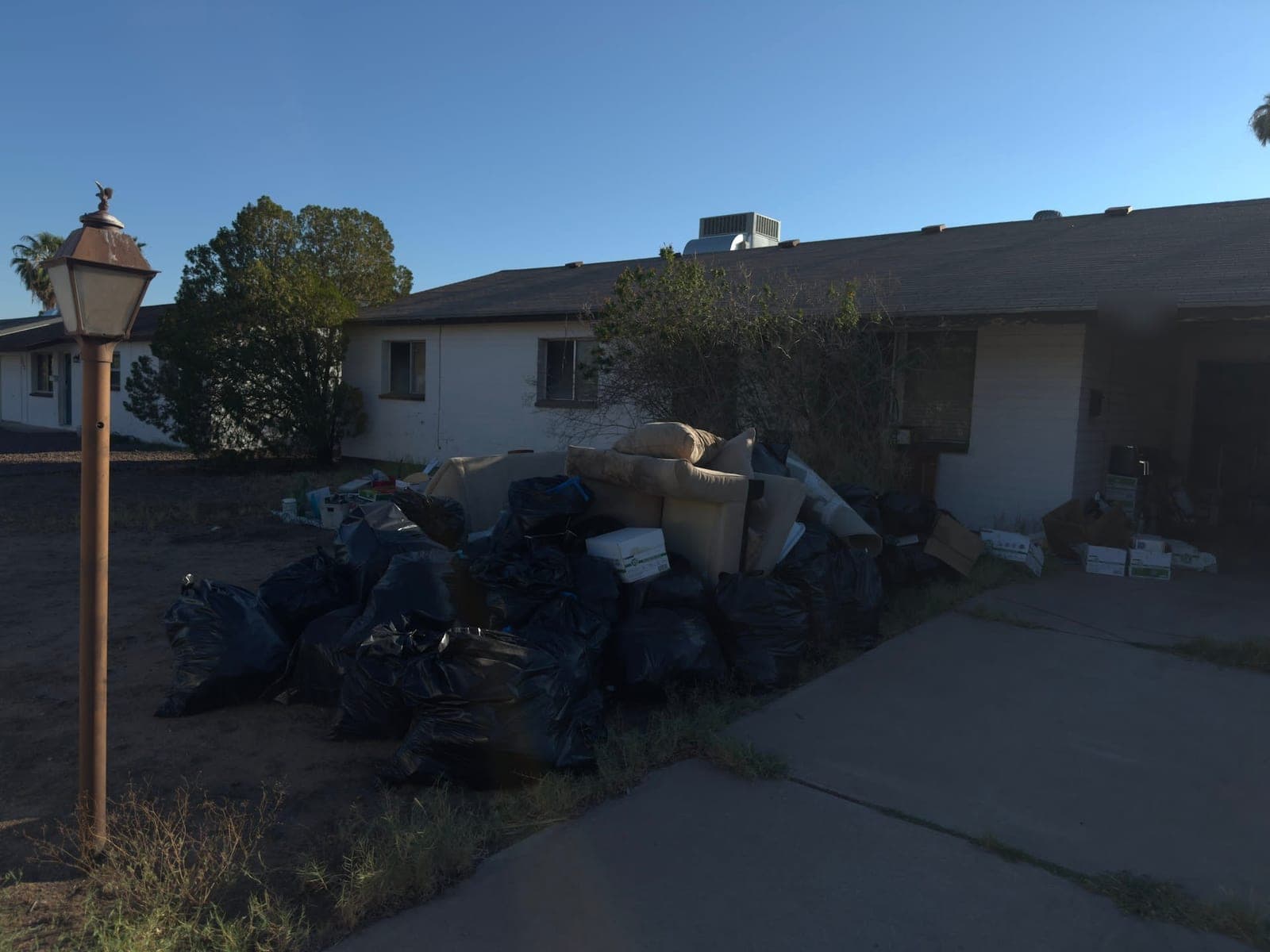 Front yard of a Tempe house with black trash bags, cushions and boxes piled up