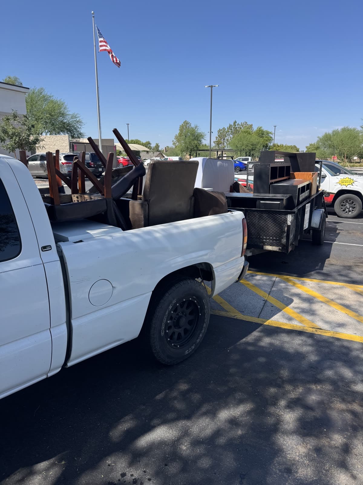Pickup truck bed loaded with chairs and furniture on a junk removal job, trailer hitched behind