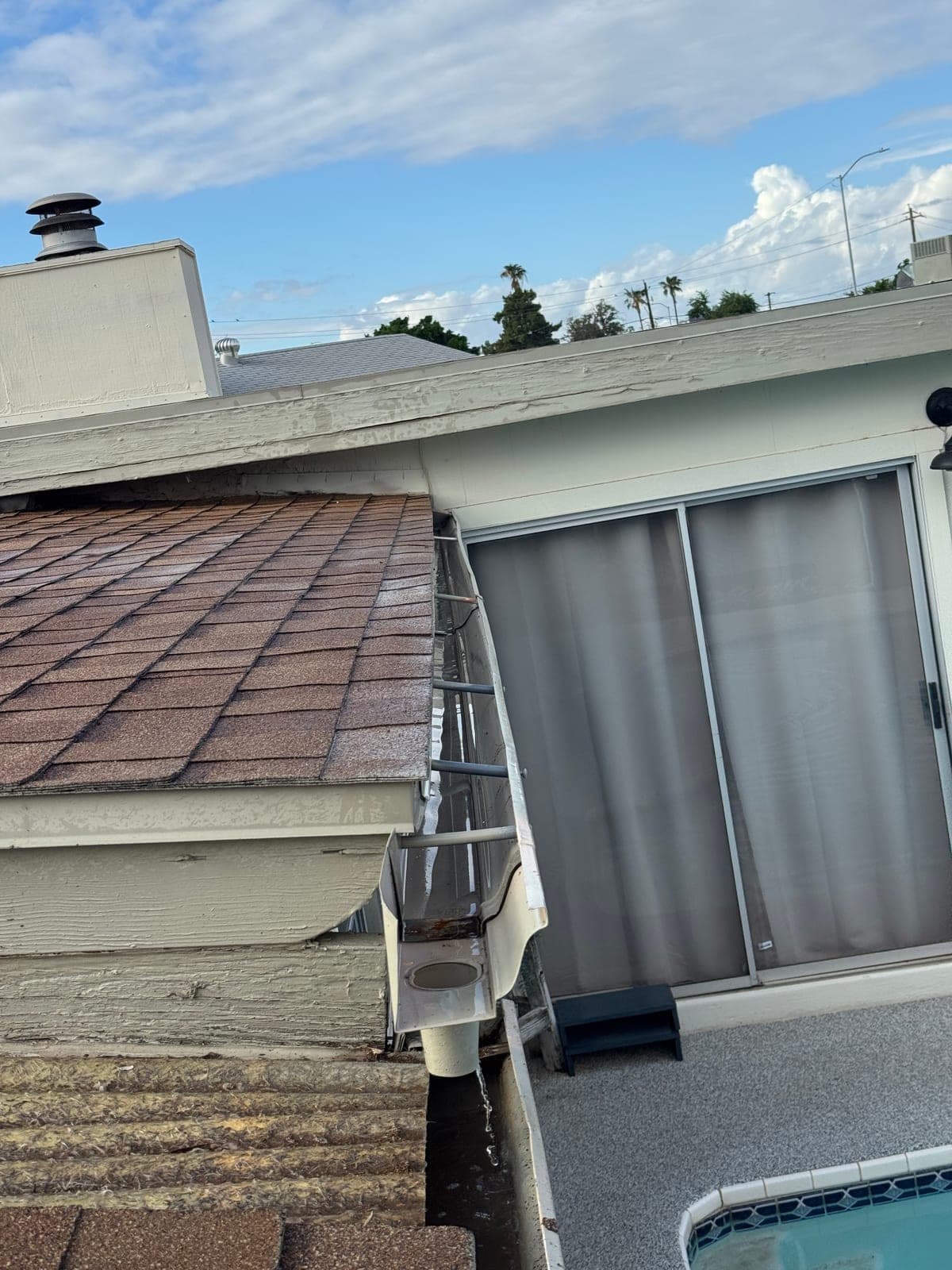 Water running clear out of a downspout outlet after a rain gutter cleaning, blue sky above the roof