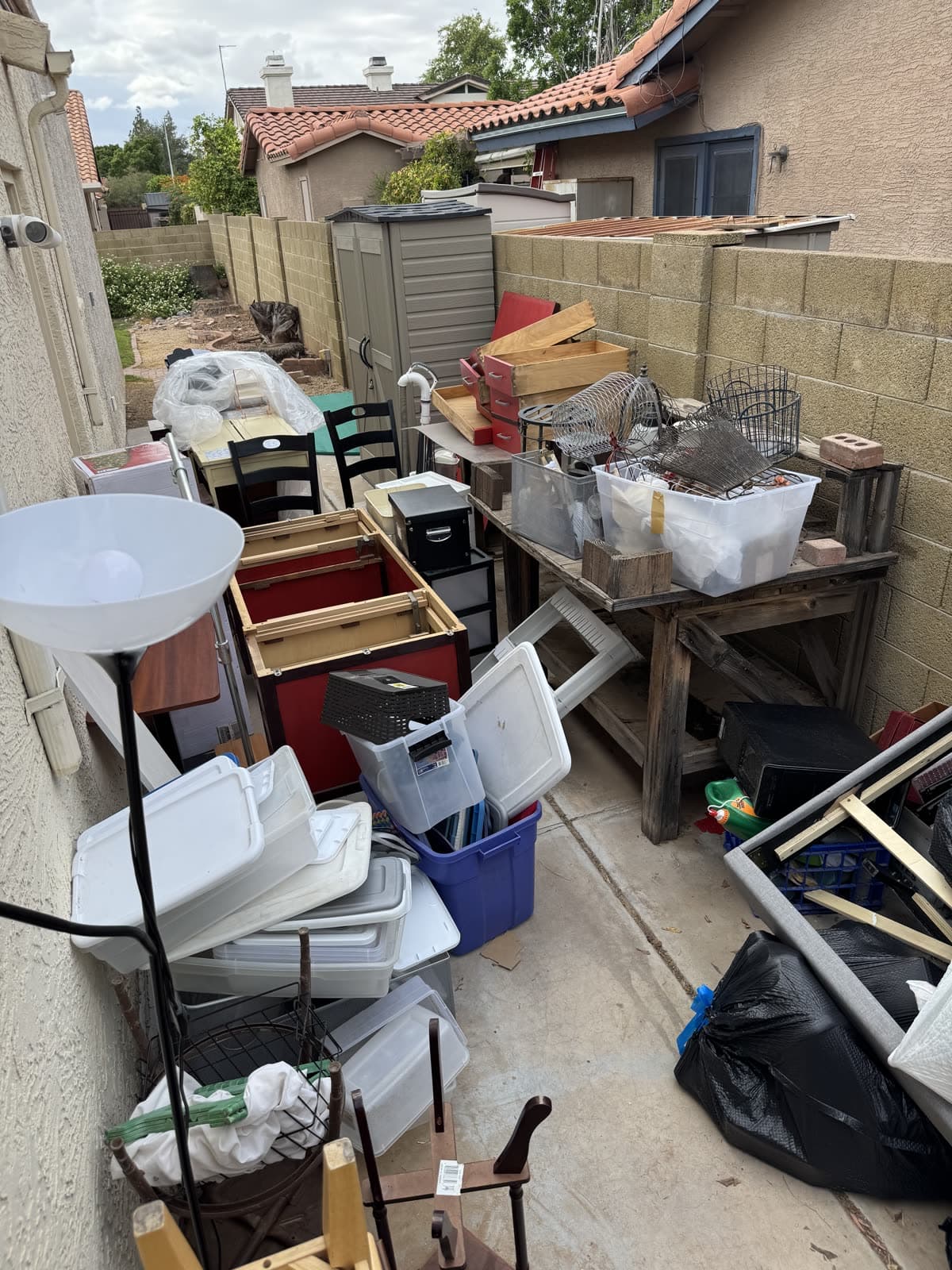 Side yard packed with storage bins, chairs, a floor lamp, and a work bench before a junk removal cleanout