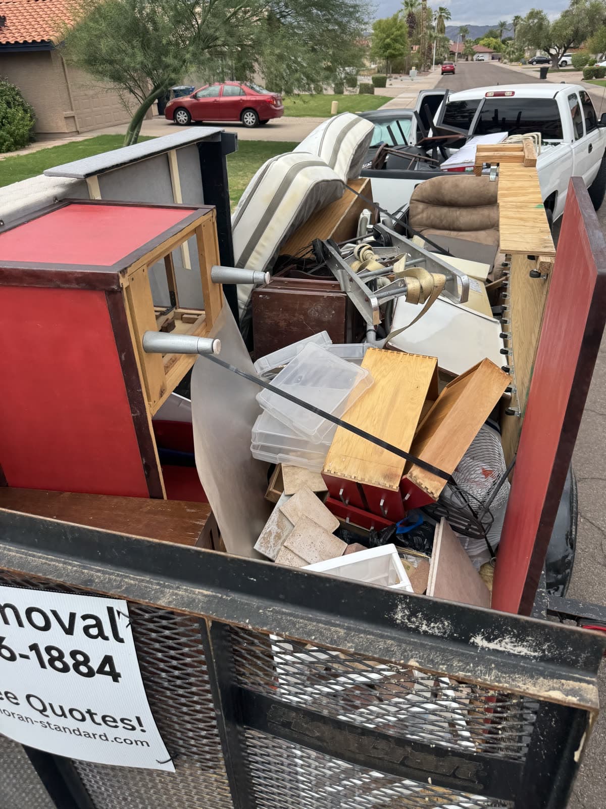 Close view of the Sonoran Standard trailer loaded on a junk removal job: red end table, patio cushions, storage bins, and drawers